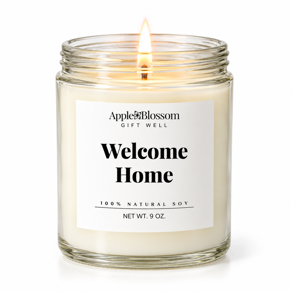 A lit 9 oz soy candle in a clear glass jar with a white label that reads 'Apple & Blossom Gift Well Welcome Home 100% Natural Soy'.